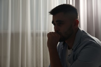 Photo of Sad man near window indoors. Space for text