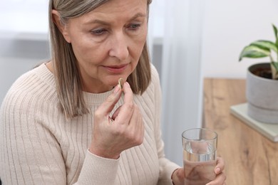 Photo of Beautiful woman taking vitamin pill at table indoors