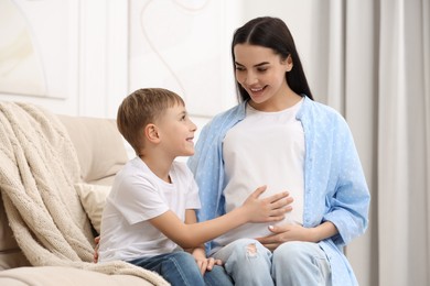 Photo of Cute boy touching pregnant mother's belly at home