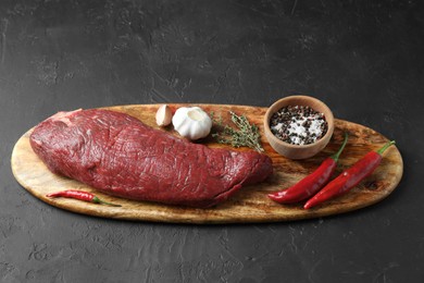 Photo of Piece of raw beef meat, products and spices on dark textured table, above view