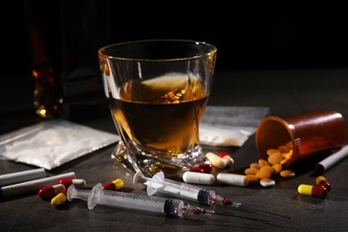 Photo of Alcohol and drug addiction. Whiskey in glass, syringes, pills, pills and cocaine on grey table