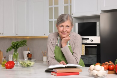 Happy woman with recipe book at table in kitchen
