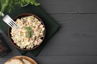 Photo of Tasty Olivier salad with boiled sausage in bowl served on grey wooden table, flat lay. Space for text