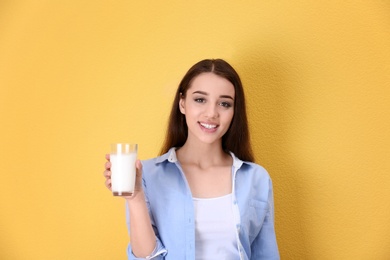 Beautiful young woman drinking milk on color background