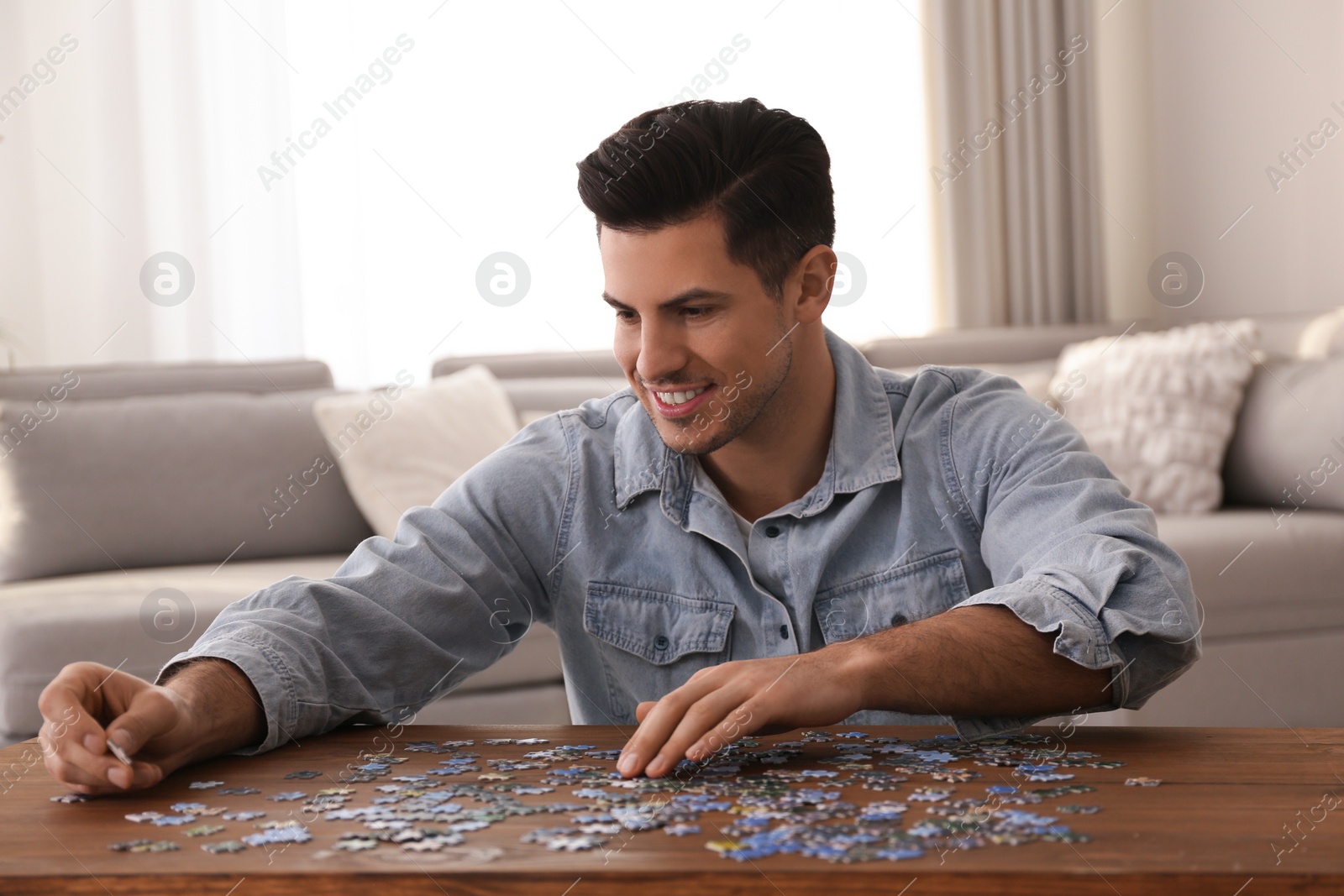 Photo of Man playing with puzzles at wooden table indoors