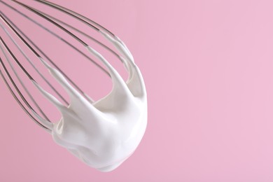 Photo of Whisk with whipped cream on pink background, closeup. Space for text