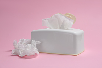 Photo of Holder with paper tissues and used crumpled napkins on pink background