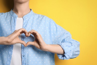 Photo of Woman making heart with hands on yellow background, closeup. Space for text
