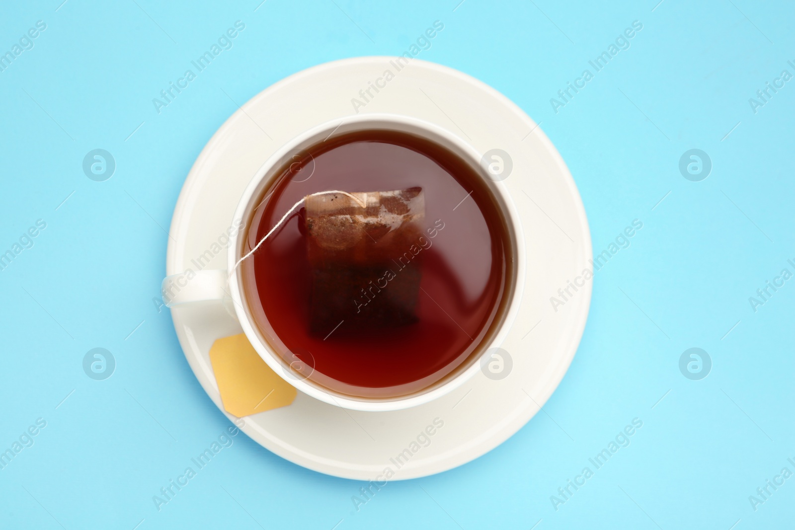 Photo of Tea bag in cup of hot water on light blue background, top view