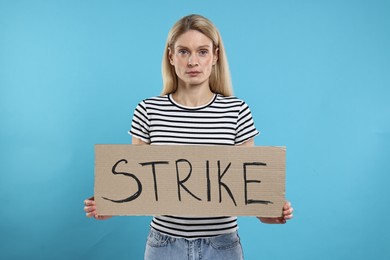 Woman holding cardboard banner with word Strike on light blue background