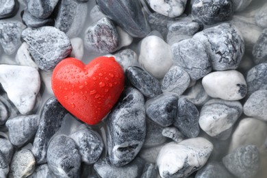 Red decorative heart on stones and water, top view. Space for text