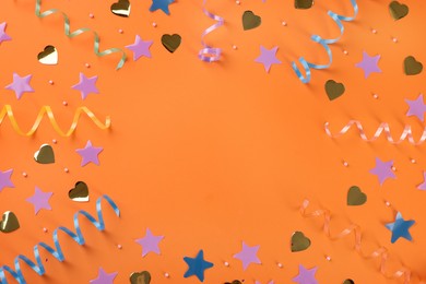 Photo of Frame of colorful serpentine streamers and confetti on orange background, flat lay. Space for text