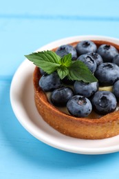 Photo of Tartlet with fresh blueberries on light blue wooden table, closeup. Delicious dessert