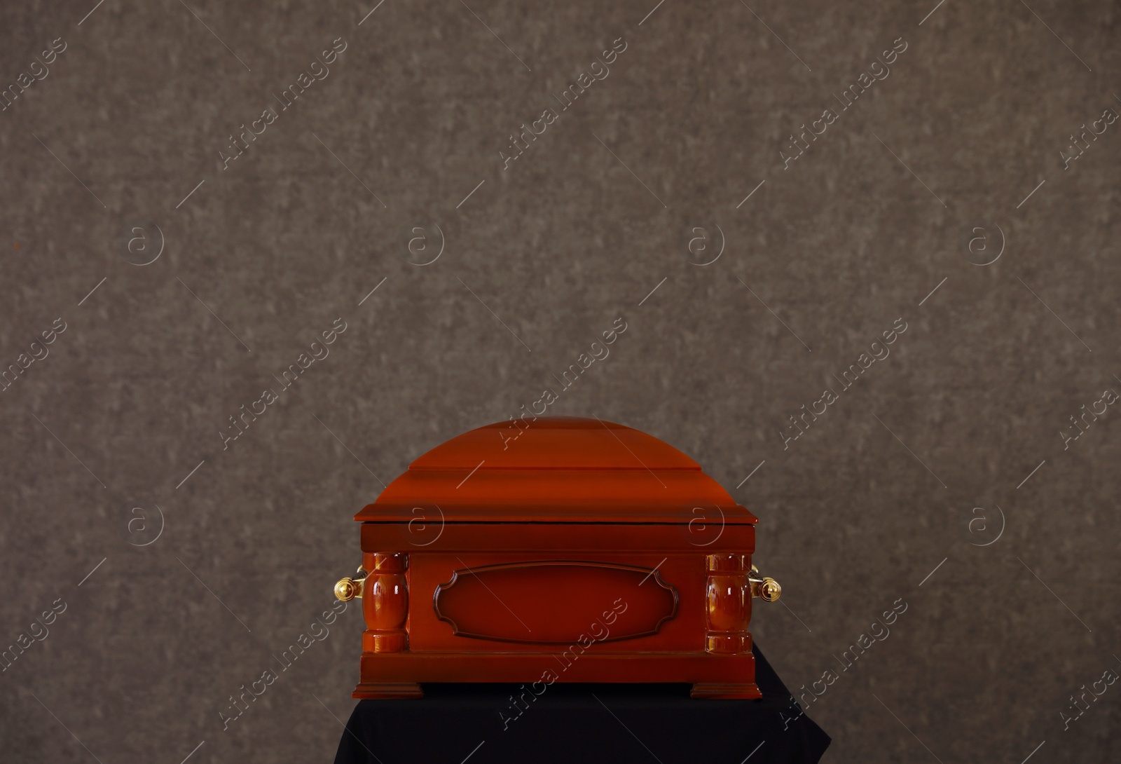 Photo of Wooden funeral casket on stand at grey wall