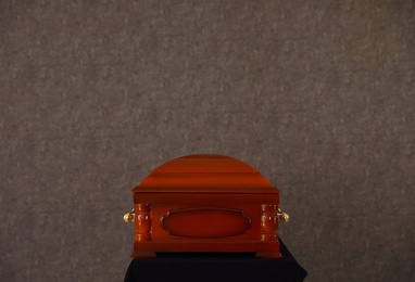 Photo of Wooden funeral casket on stand at grey wall
