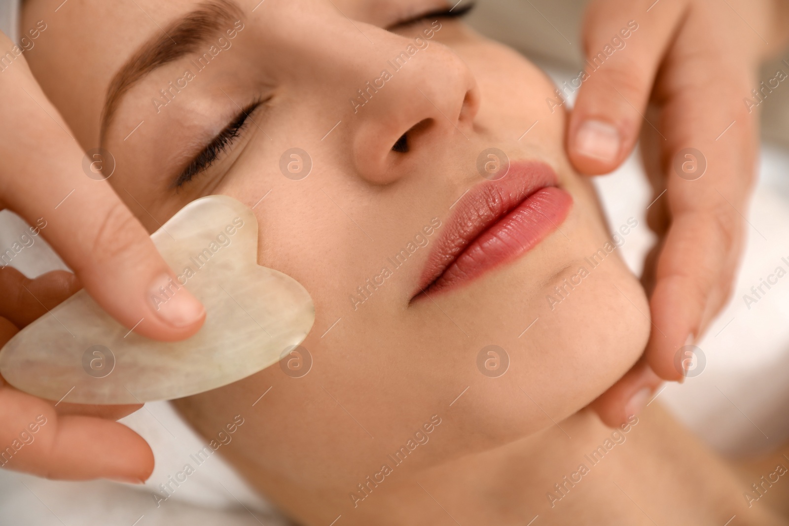 Photo of Young woman receiving facial massage with gua sha tool in beauty salon, closeup