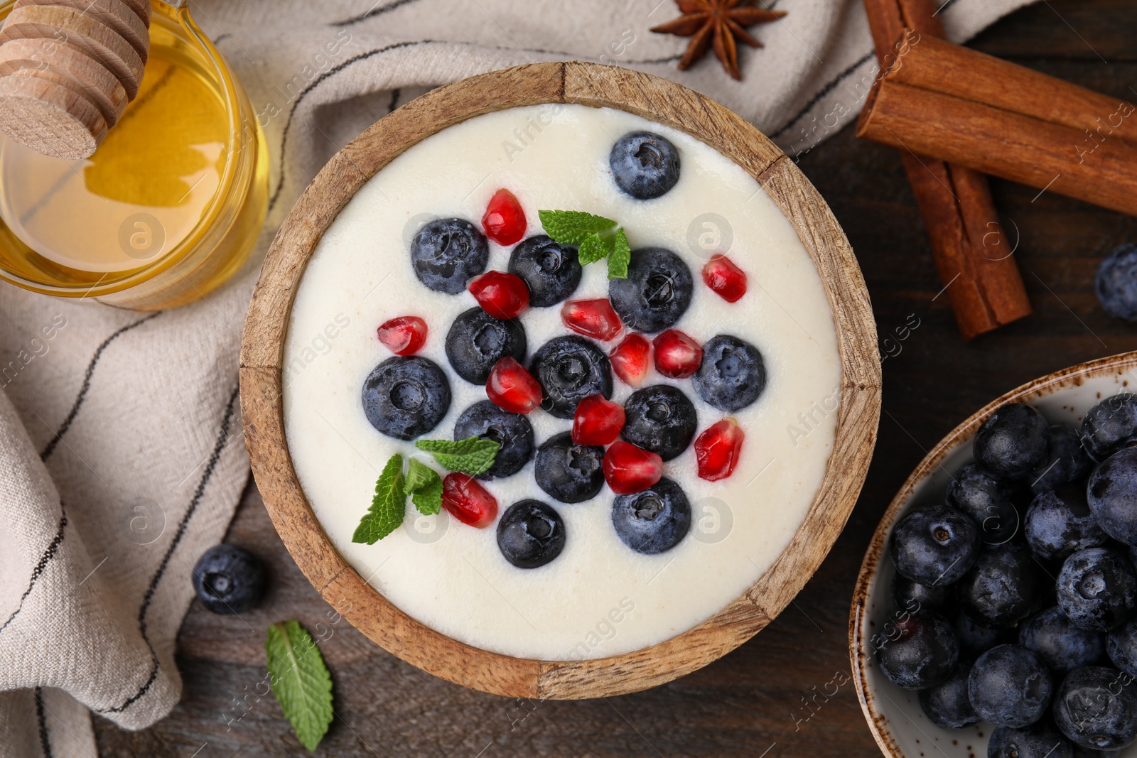 Photo of Bowl of delicious semolina pudding with blueberries, pomegranate and ingredients on wooden table, flat lay