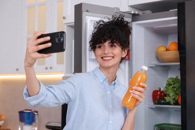 Photo of Smiling food blogger with bottle of juice taking selfie near fridge in kitchen