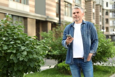 Photo of Portrait of handsome mature man using mobile phone in city. Space for text