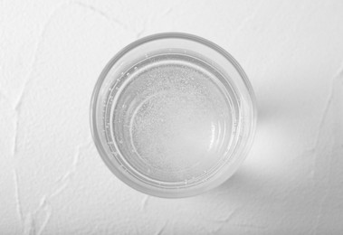 Glass of soda water on white table, top view