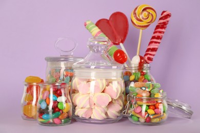 Jars with different delicious candies on violet background