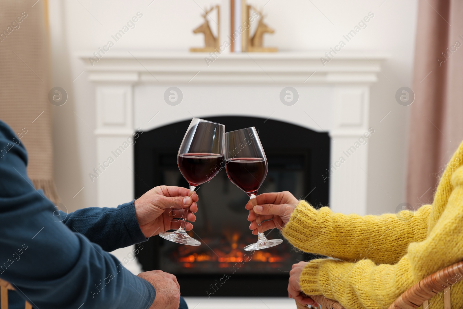Photo of Lovely couple with glasseswine spending time together near fireplace at home, closeup