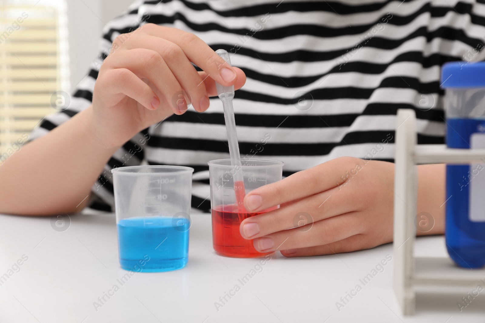 Photo of Girl mixing colorful liquids at white table indoors, closeup. Chemical experiment set for kids