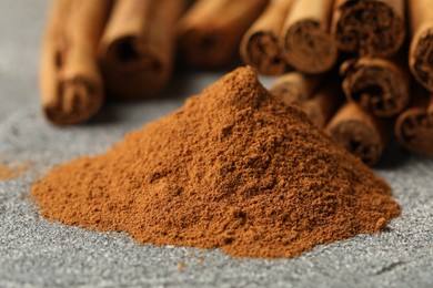 Cinnamon powder and sticks on grey table, closeup