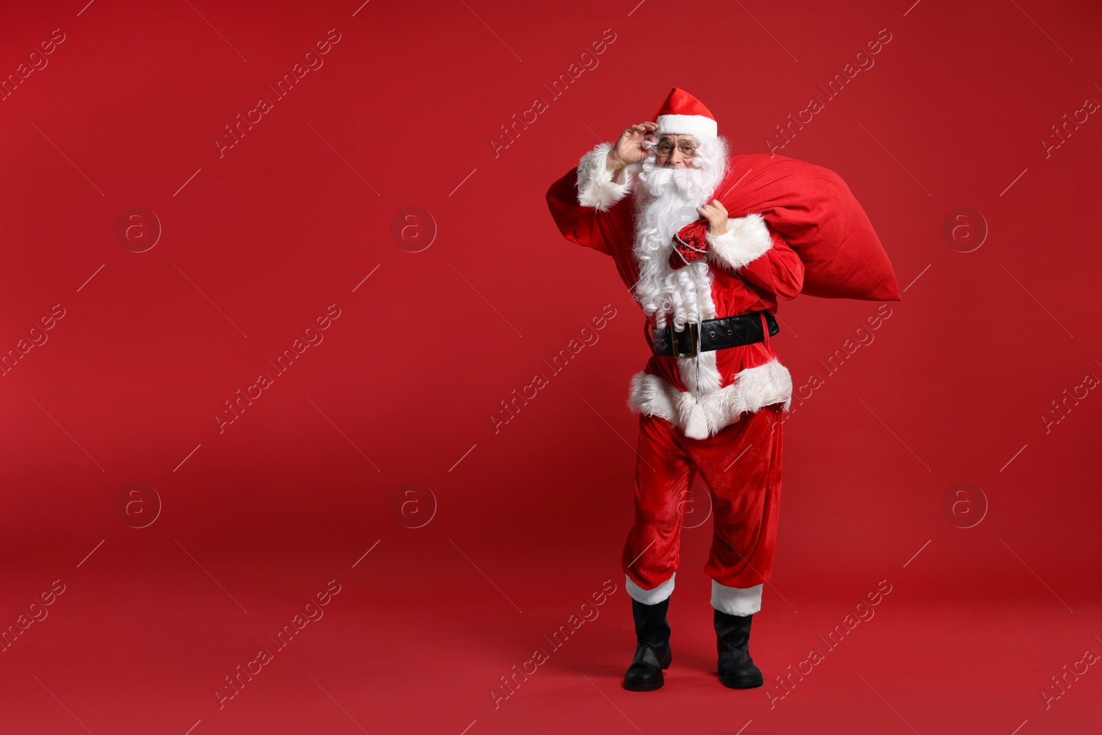 Photo of Santa Claus with bag of Christmas presents posing on red background, space for text