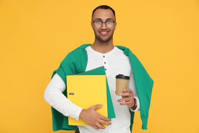 Photo of Happy young intern holding notebooks, cup of hot drink on orange background