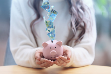 Image of Woman with piggy bank at table indoors, closeup