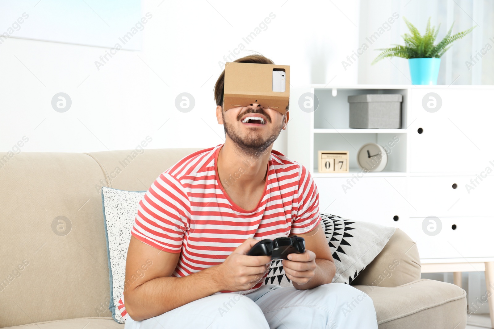 Photo of Young man using cardboard virtual reality headset at home