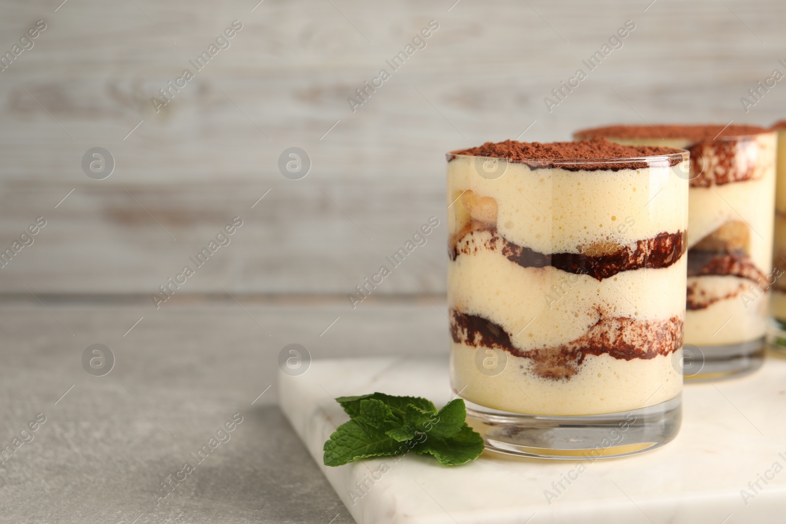 Photo of Delicious tiramisu in glasses and mint on grey textured table, closeup. Space for text