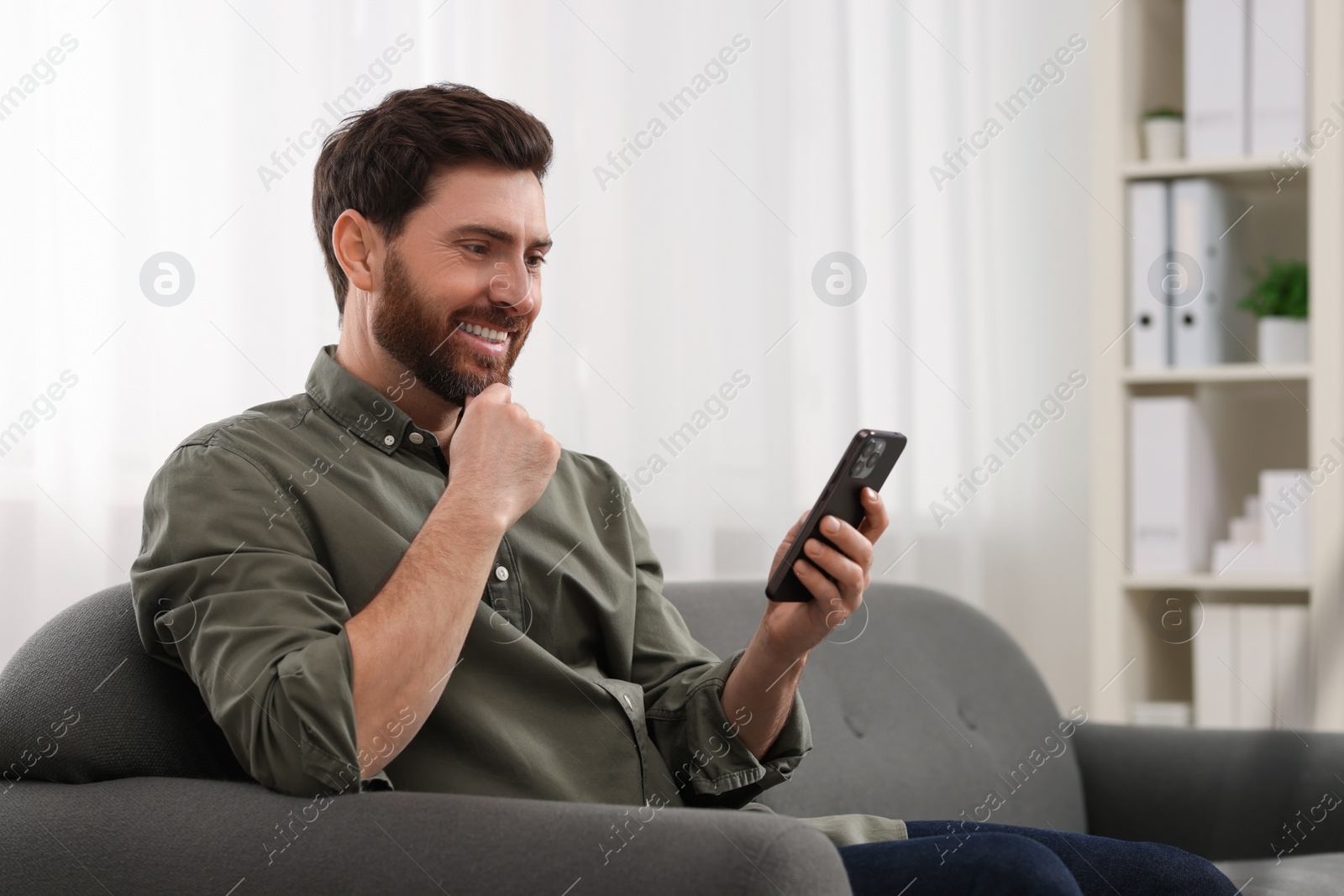 Photo of Smiling man using smartphone on sofa at home