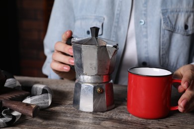 Brewing coffee. Woman with moka pot and cup at wooden table, closeup
