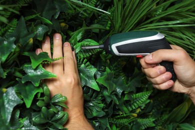 Photo of Man with screwdriver installing green artificial plant wall panel, closeup