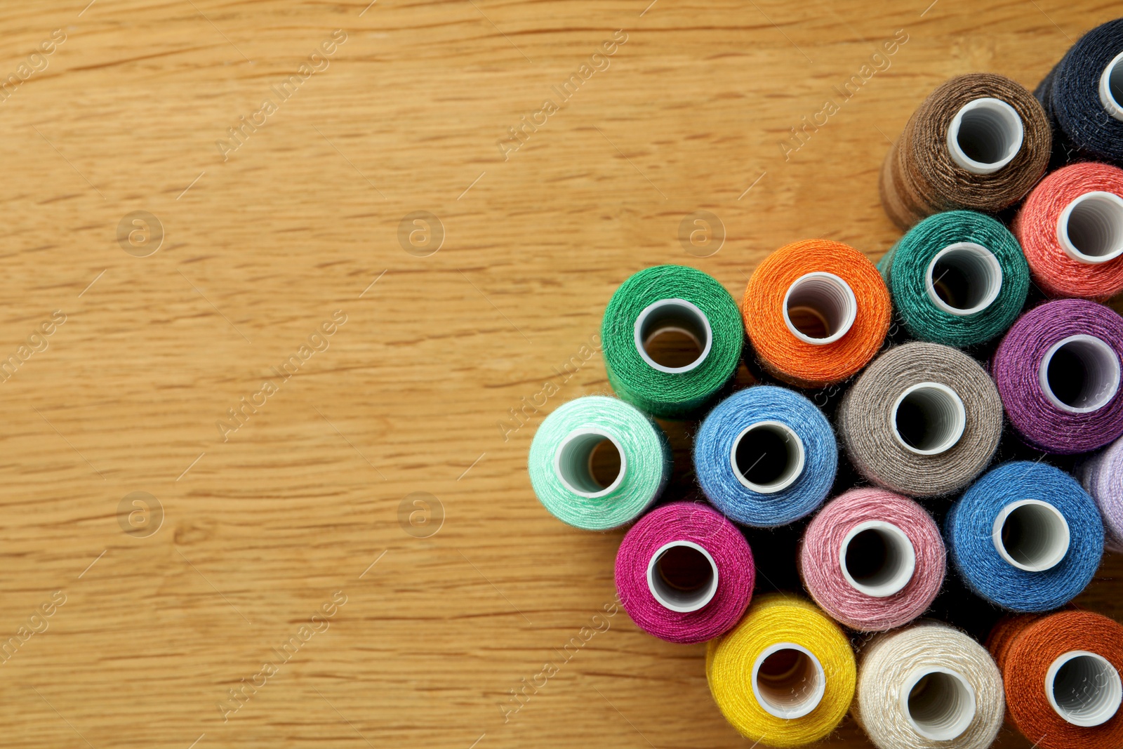 Photo of Many colorful sewing threads on wooden table, flat lay. Space for text