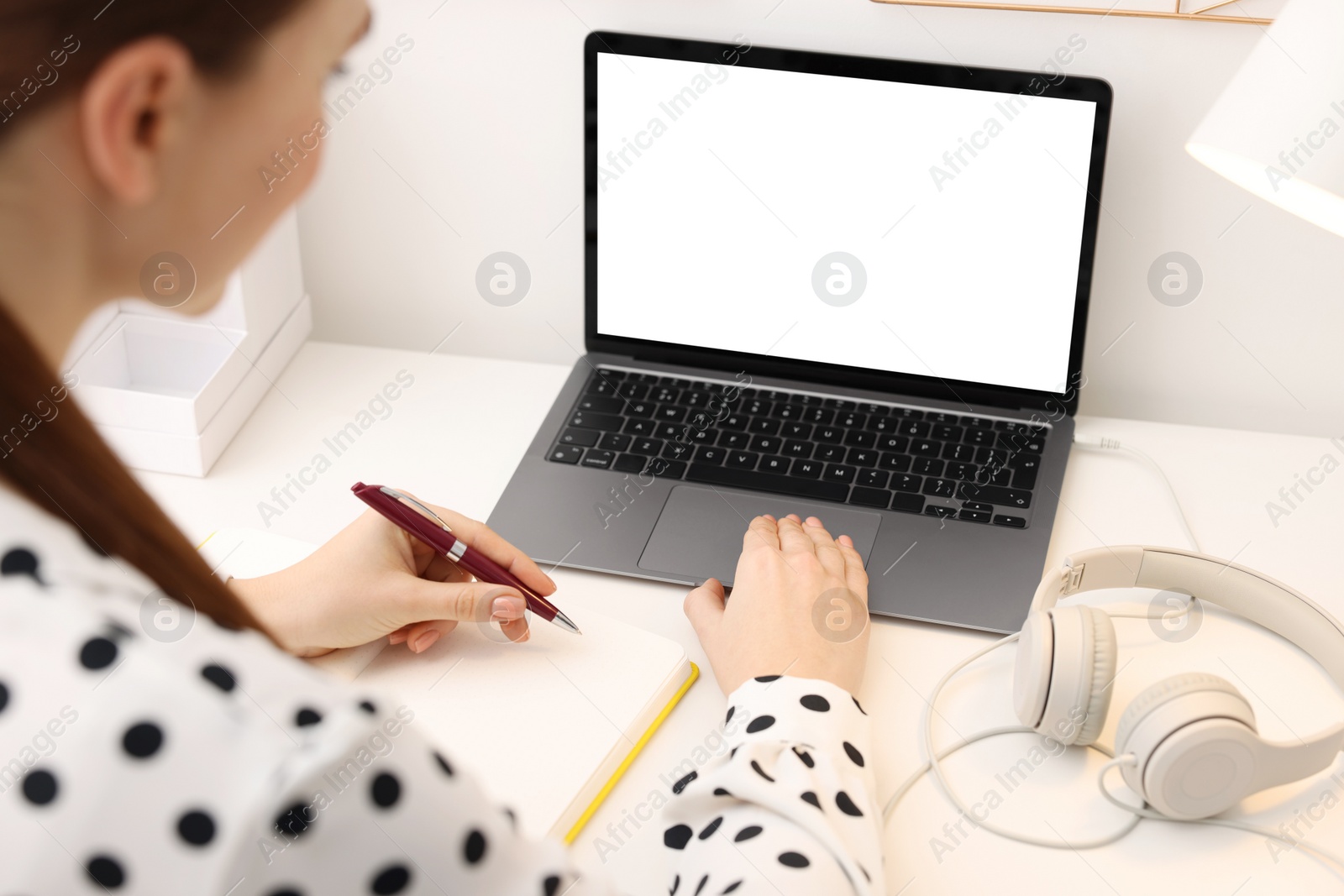 Photo of E-learning. Woman taking notes during online lesson at table indoors, closeup