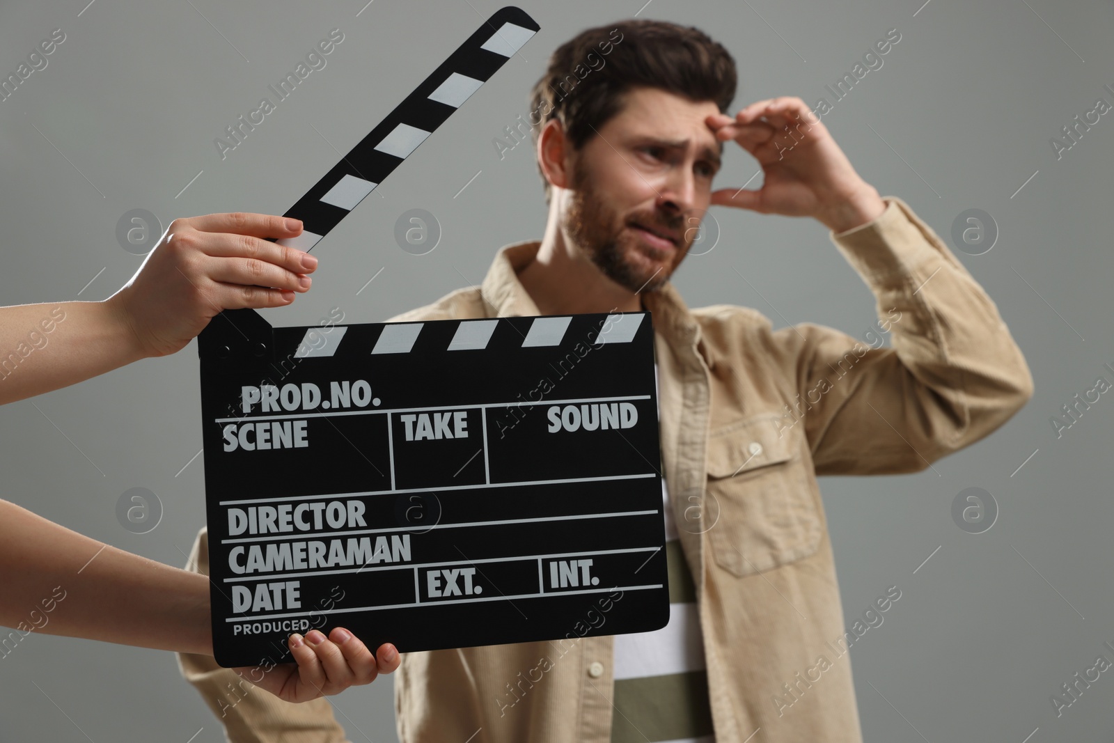 Photo of Emotional actor performing while second assistant camera holding clapperboard on grey background, closeup