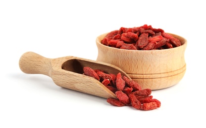 Wooden bowl and scoop of tasty dried goji berries on white background