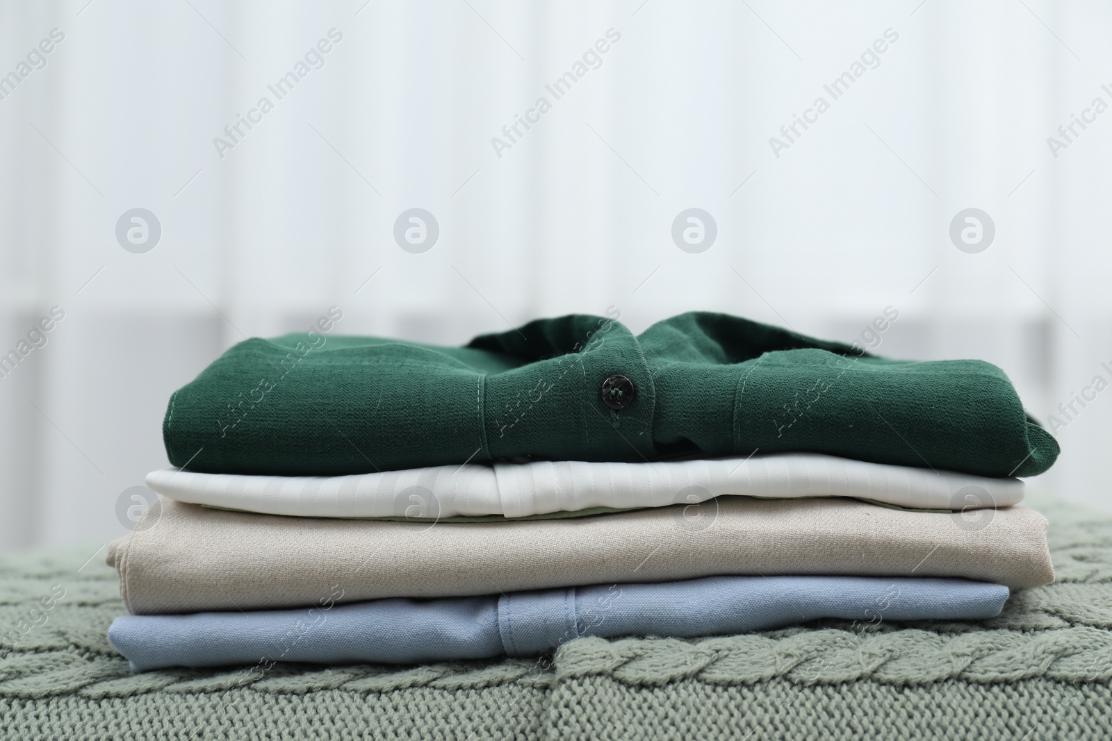 Photo of Sorting and organizing. Stack of different folded clothes on bed indoors