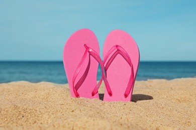 Photo of Stylish pink slippers on sand near sea. Beach accessory