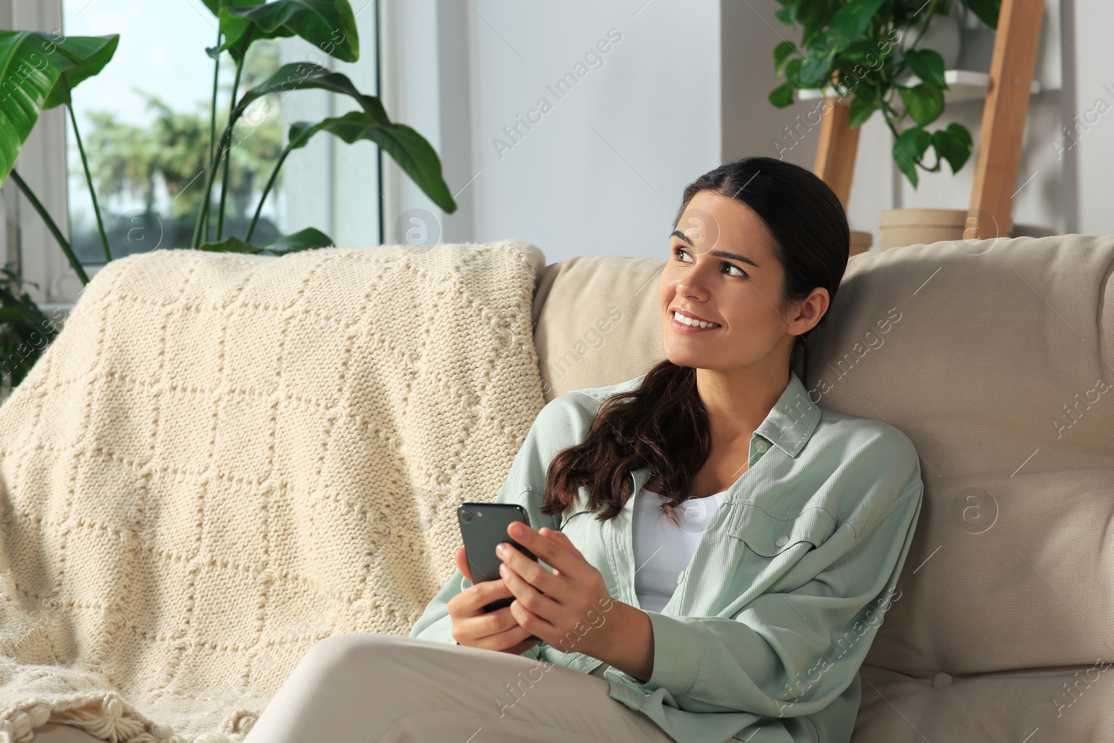 Photo of Young woman with smartphone sitting on sofa at home