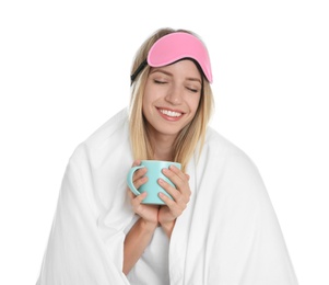 Happy woman in sleeping mask wrapped with blanket holding cup on white background