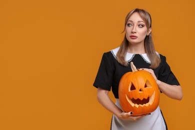 Photo of Woman in scary maid costume with carved pumpkin on orange background, space for text. Halloween celebration