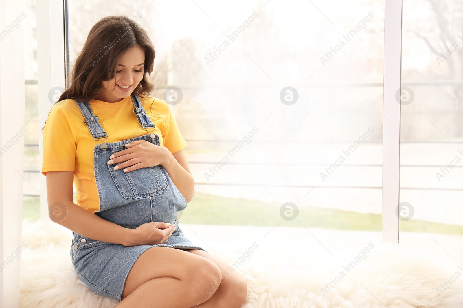 Photo of Beautiful pregnant woman sitting near window at home