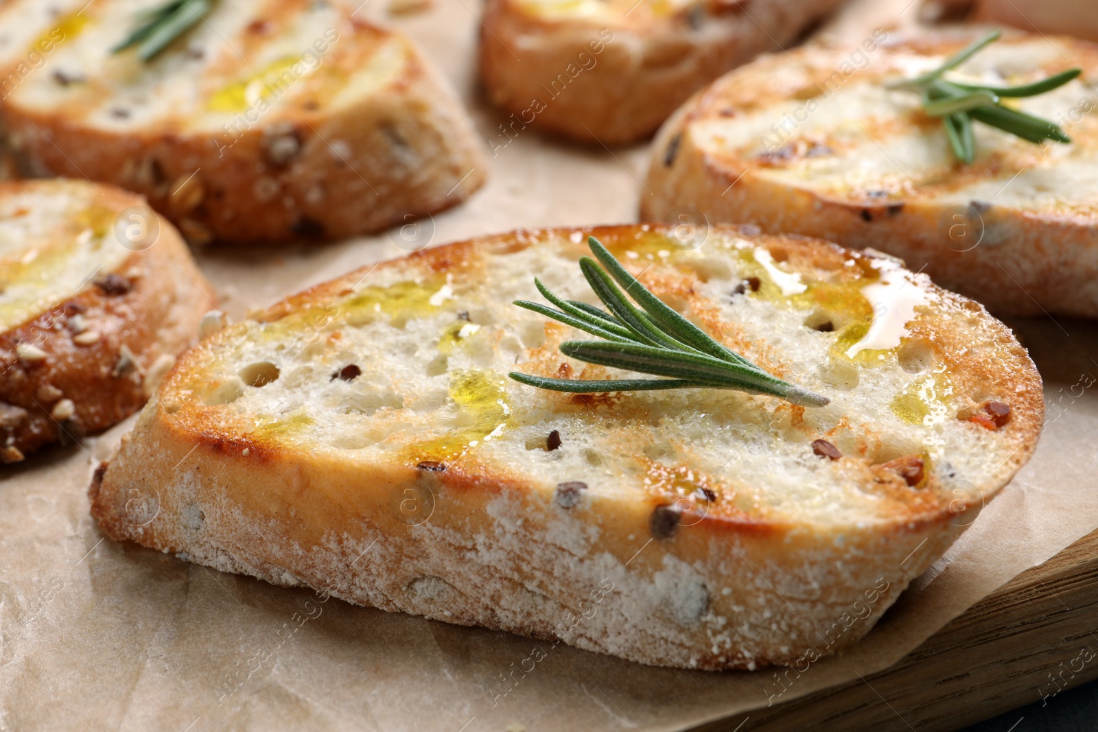 Photo of Tasty bruschettas with oil and rosemary on parchment paper, closeup