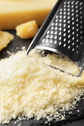 Photo of Pile of grated parmesan cheese and grater on black table, closeup