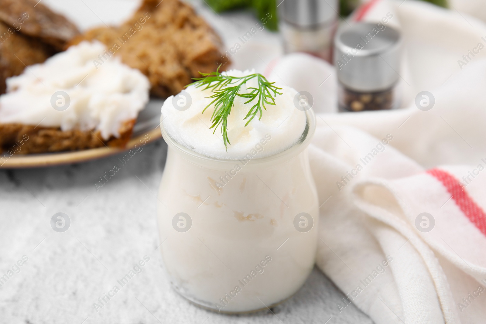 Photo of Delicious pork lard with dill in glass jar on light textured table, closeup