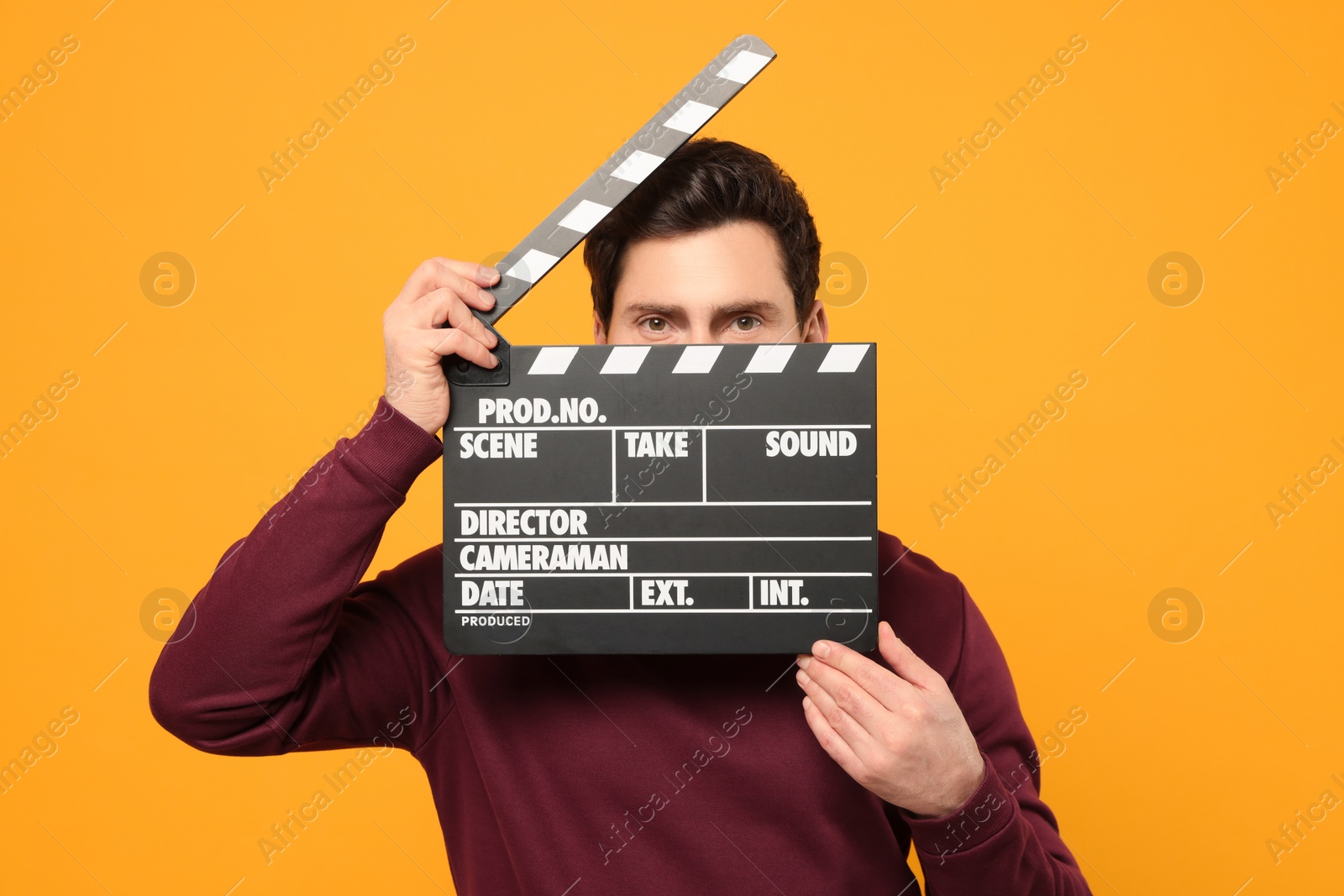 Photo of Adult actor holding clapperboard on orange background